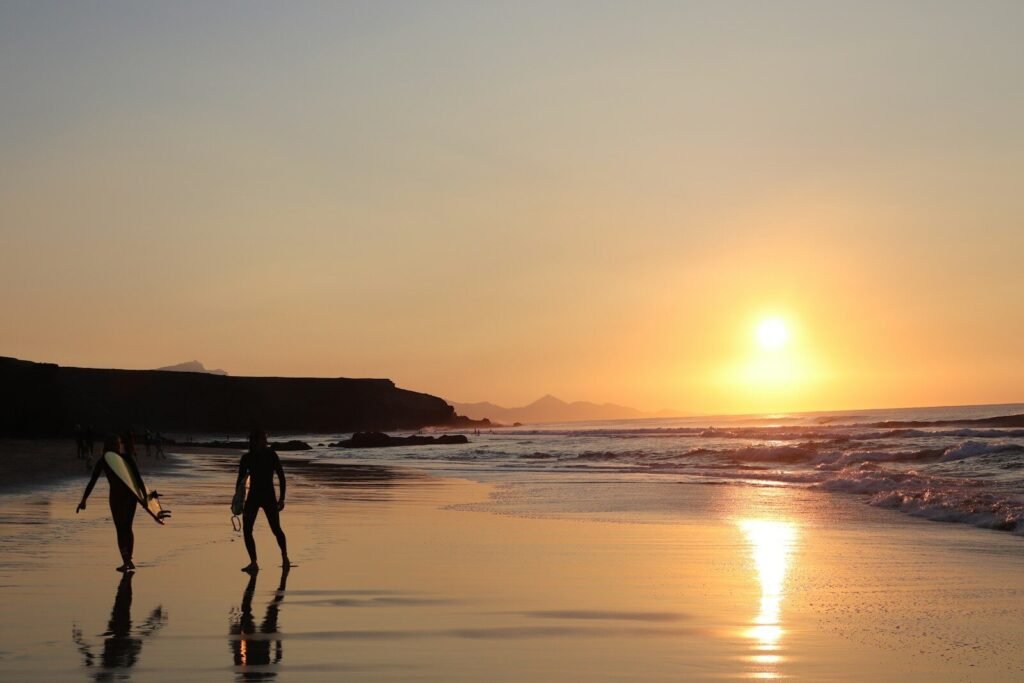 two people walking on the beach at sunset